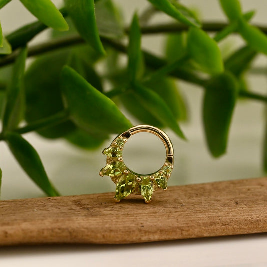 Gold earring with green gemstones on a wooden surface with a green leafy background