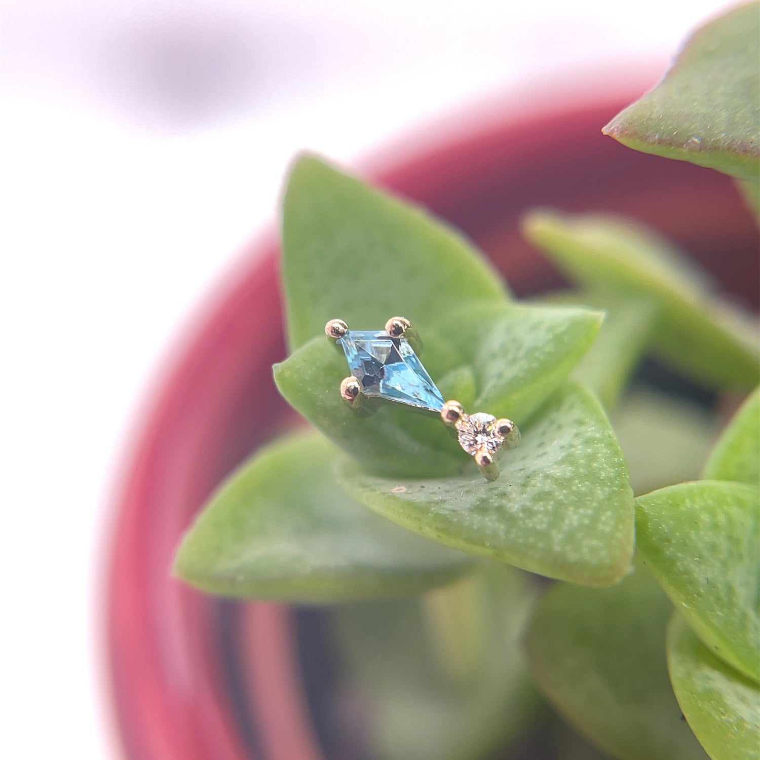 This beautiful kite shaped Swiss blue topaz is accented by a brilliant white diamond below. The fun prong settings on this unique piece creates a delicate yet stunning piece of jewelry you can wear in a variety of ear locations or a nostril.